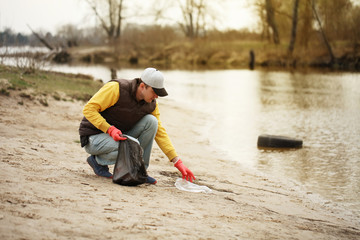 Man volunteer lift off garbage in beach. Coastline environment pollution, outdoor trash and rubbish.