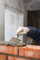 Hand with a trowel, in the process of laying a wall of red brick.