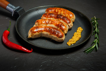 closeup fried sausages on round black pan with granular mustard