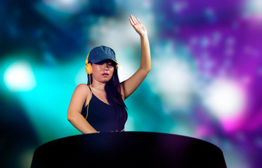 young attractive and happy Asian Chinese DJ woman remixing using deejay gear and headphones at night club with lights background in clubbing fun and music concept