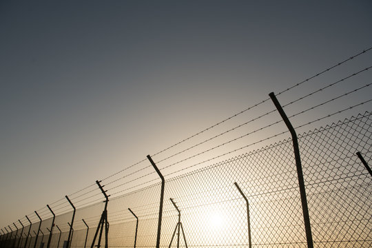 Metal security fence located in front of cloudless sky with bright sun