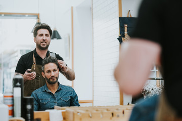 From below barber combing hair of handsome stylish male sitting in barbershop