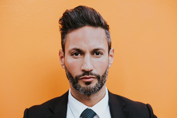 Adult handsome elegant businessman in formal suit looking at camera near orange wall