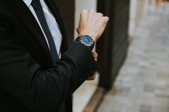 Crop Elegant Businessman In Formal Suit Showing Watch On Blurred Background