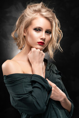 Fototapeta premium Beautiful young braless slim blonde girl with disheveled hair and aggressive makeup, wearing an unbuttoned shirt and jeans emotionally posing on a gray background. Commercial design