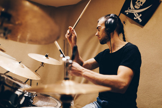 Positive handsome male with headphones playing on drums in studio
