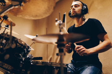 Positive handsome male with headphones playing on drums in studio