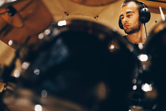 Positive handsome male with headphones playing on drums in studio
