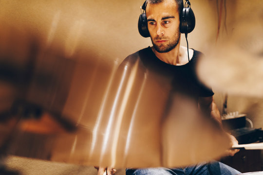 Positive handsome male with headphones playing on drums in studio