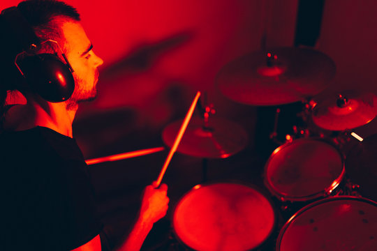 Side view of crop male holding drumsticks and playing on drums in redness