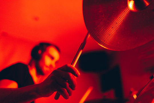 Side view of crop male holding drumsticks and playing on drums in redness