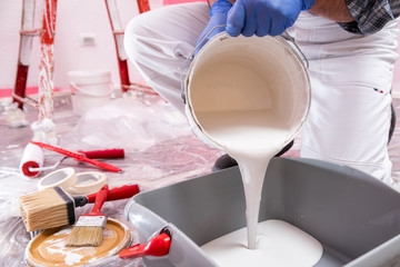 Caucasian house painter worker in white overalls, pour the white paint into the container. Construction industry. Work safety.