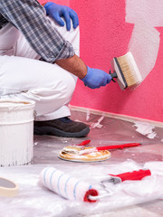 Caucasian house painter worker in white overalls, with the brush painting the pink wall with white paint. Construction industry. Work safety.