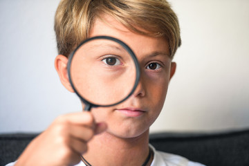 happy blond boy looking through a magnifying glass. concept of curiosity with respect to life, search for details and clues, investigating, digging observe