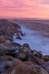 Beautiful pink sunset in the seaside with waves crushing over the rocky coast