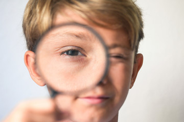 happy blond boy looking through a magnifying glass. concept of curiosity with respect to life, search for details and clues, investigating, digging observe, focus on the open eye