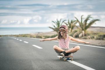 Young blond boy plays aviator sitting cross-legged on skateboard with arms outstretched to fly smiling child imitates plane flying on airport runway. Concept image of a plane taking off for a vacation - Powered by Adobe
