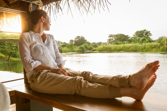 Side view of barefoot female sitting in gazebo and looking at tranquil pond on sunny day in Sri Lanka
