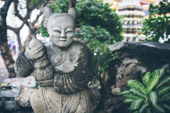 Beautiful weathered statuette placed near rocks and green tropical plants in amazing garden on sunny day in Thailand