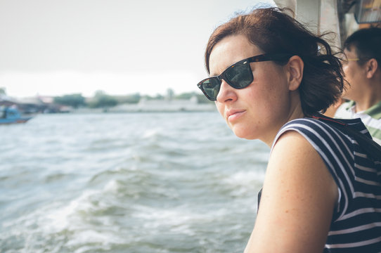 Side view of female in sunglasses looking at stormy sea while traveling on modern vessel in Thailand