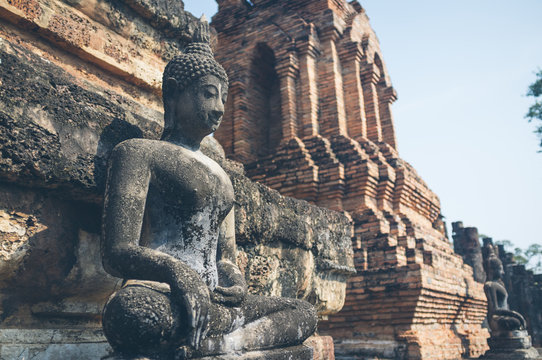 Weathered statue of Buddha located near shabby stone walls of ancient oriental temple in Thailand