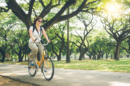 Pretty female in casual outfit riding modern bike on path near green trees in beautiful park on sunny day in Thailand