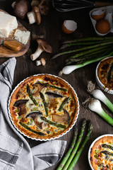 Baked homemade quiche pie with asparagus and mushrooms in white ceramic form on wooden background, Flat lay