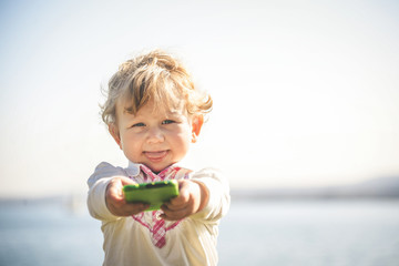 Cute little girl using modern smartphone. Baby holding mobile phone and taking funny selfie with cellphone camera. Child learning how to use modern electronic devices. Children and technology concept