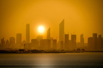 Fototapeta na wymiar Golden hour on the skyline of a modern city. Sunrise over high buildings near the ocean in UAE. Beautiful sky line of a big new arabian metropole. Sunset on a urban landscape in the middle east