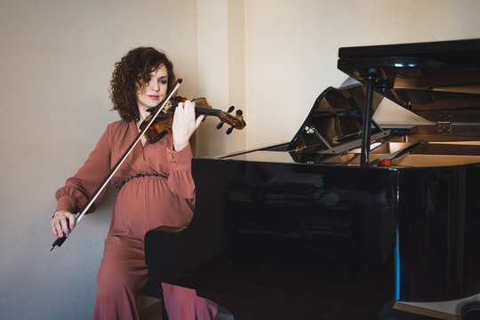 Woman sitting next to a piano playing a violin
