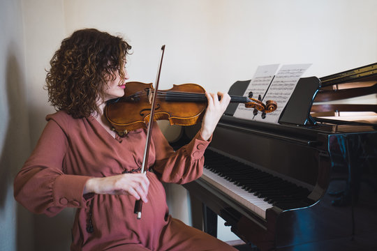 Woman sitting next to a piano playing a violin