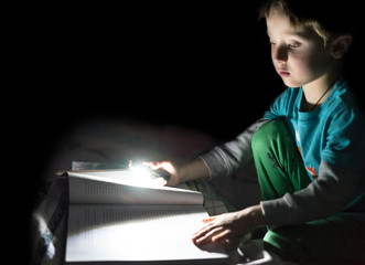 Fun boy reading a book with flashlight in the hand at home at night