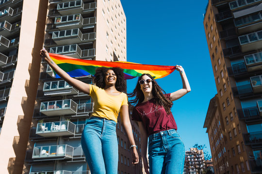 Portrait of smiling couple holding rainbow flag against building