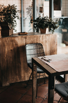 Stylish table and comfortable chair located ear shabby cabinet with potted plants in cozy room