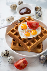 Close-up of belgian waffles served with fried quail eggs and tomatoes, vertical shot
