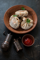 Ceramic plate with georgian meat dumplings khinkali, vertical shot on a dark brown stone background