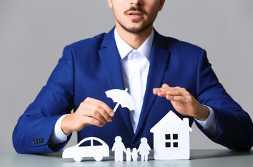 Male insurance agent covering paper family, car and home with umbrella cutout at table, closeup