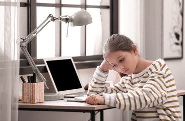 Pretty preteen girl doing homework at table in room