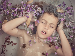 From above face of child in liquid between fresh petals of blooms