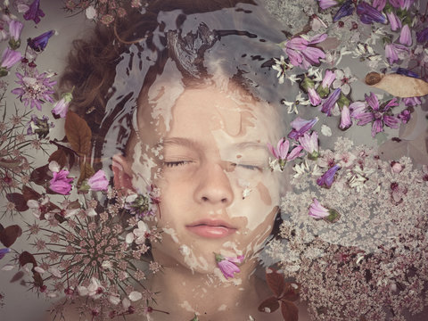 From above face of child in liquid between fresh petals of blooms