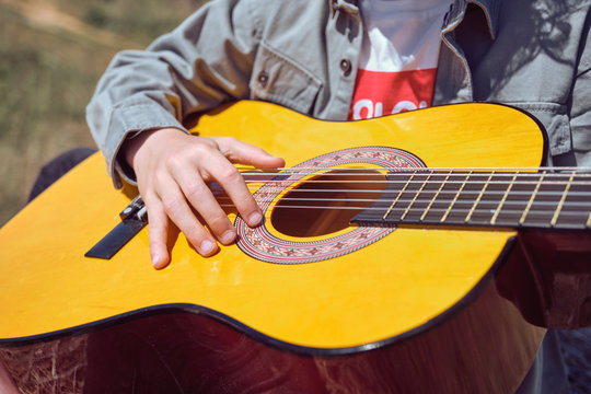 Hand of anonymous kid playing acoustic guitar on blurred background of meadow on sunny day in countryside