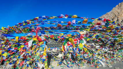 Die wehenden Fahnen an der Spitze des Thorung La Pass, Annapurna Circuit Trek, Nepal. Herzlichen Glückwunsch für die Mühe. Bunte Gebetsfahnen, die an der Steinmauer befestigt sind, wehen vom Wind. Klarer Himmel.