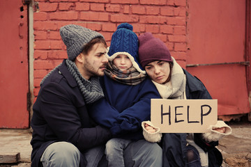 Poor young family with HELP sign on dirty street