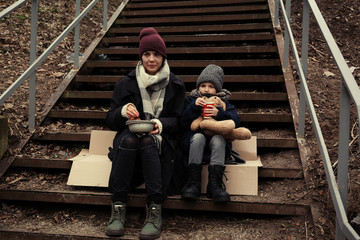 Poor mother and daughter with bread sitting on stairs outdoors