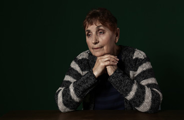 Poor senior woman sitting at table against color background. Space for text