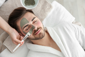 Cosmetologist applying mask on client's face in spa salon, above view