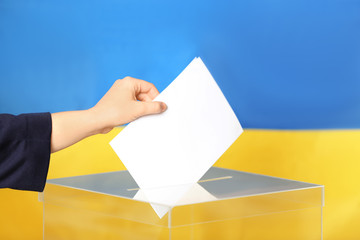 Woman putting voting paper into ballot box against Ukrainian flag, closeup