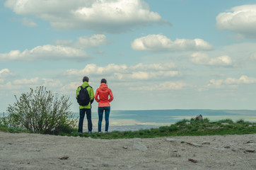 couple on a background of blue sky with clouds standing on a hill and looking into the distance