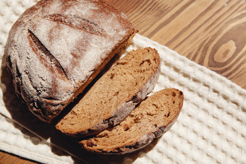 Loaf of fresh bread with slices on wooden background with sunshine, top view 