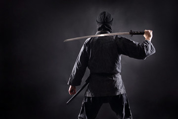 Ninja samurai with katana stands with his back to the viewer. - obrazy, fototapety, plakaty
